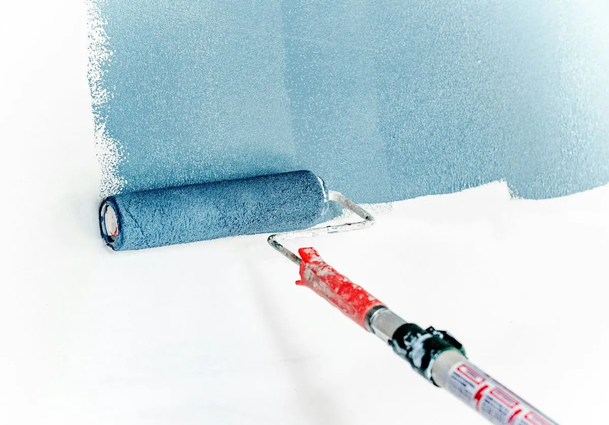 Rouleau de peinture bleu en cours d'application sur un mur blanc