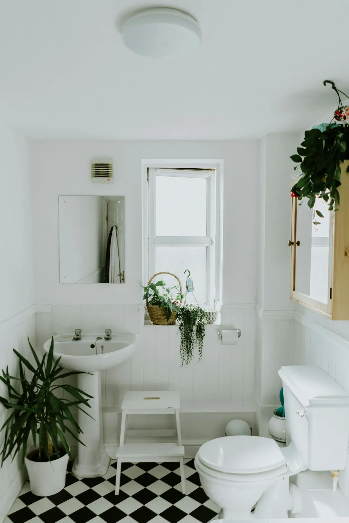 Salle de bain blanche rénovée avec WC, lavabo colonne et carrelage damier au sol